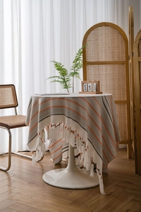 Close-up of bohemian table cloth with orange and black stripes and white fringe trim
