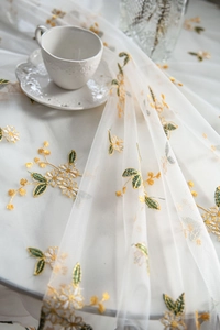 Detail of white mesh lace tablecloth with yellow flower embroidery and coffee set