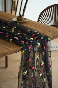 Detail of black mesh table runner with colorful floral embroidery on a wooden table
