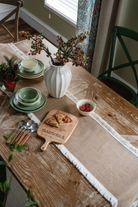 Detail of rustic dining set with ceramic plates, wooden pizza peel and jute table runner