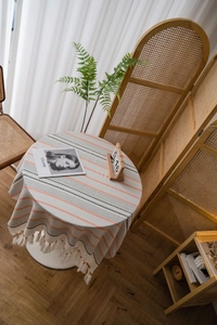 Close-up of beige round cotton linen tablecloth with orange stripes and handmade tassels