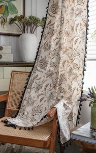 Detail of floral print linen curtain with black tassel fringe in a rustic farmhouse style