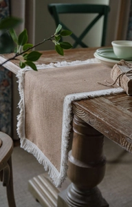 Detail of natural jute table runner with white fringe on a rustic wooden table top