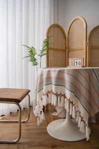Detail of woven table cover with orange stripes and fringe trim in a cozy setting
