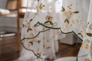 Detail of yellow flower embroidery on white sheer fabric with green wavy scalloped edges