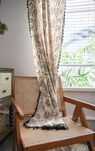 Detail of floral printed curtain with black fringe tassels on a wooden chair