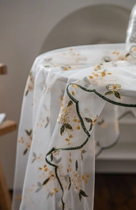 Detail of white mesh lace tablecloth with yellow floral embroidery and green scalloped edges