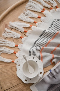 Detail of bohemian woven tablecloth with orange geometric patterns and handmade tassels