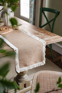 Detailed close-up of natural jute table runner with white tassel edges on wooden table