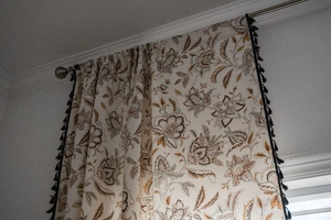 Close-up of floral print curtain with elegant black tassel trim on cotton linen fabric