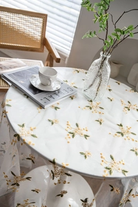 Close-up of white lace tablecloth with yellow and green flower embroidery on a round table
