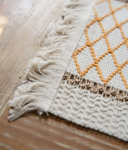 Detail shot of boho jute placemat featuring orange geometric patterns and cotton tassels
