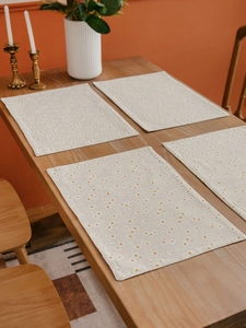 Set of four cotton linen placemats with white daisy floral prints on a wooden table