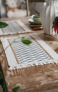 Dettaglio della tovaglietta intrecciata geometrica con eleganti nappe su tavolo in legno