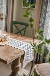Dettaglio del runner da tavola boho in cotone e lino con motivi a rombi neri e nappe