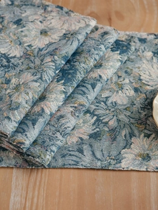 Detail of blue and beige floral jacquard placemat showing thick fabric texture on wood