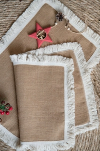 Close-up of natural burlap table mats with white fringe trim and festive pinecone decor