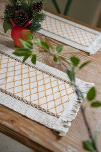 Close-up of bohemian cotton table runner with yellow diamond weave and tassel edge