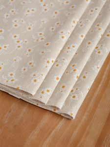 Close-up of linen place mat with daisy print on a rustic wooden table surface