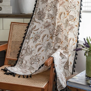 Vintage floral cotton linen curtain with black tassel fringe on a rustic wooden chair