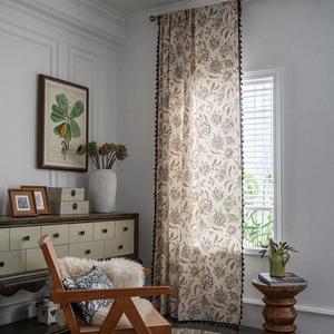Floral American country curtains with black pompom fringe trim in a cozy sunlit room