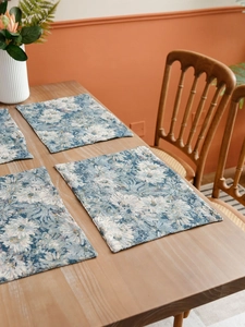 Close-up of blue and white jacquard floral placemats on a light wooden table