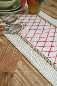 Detail of red geometric diamond embroidery on linen table runner with woven tassels