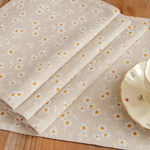 Daisy print linen placemats stacked on a wooden table with vintage floral ceramic plates