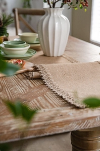 Detail of natural jute table runner with woven lace edges on a wooden table setup