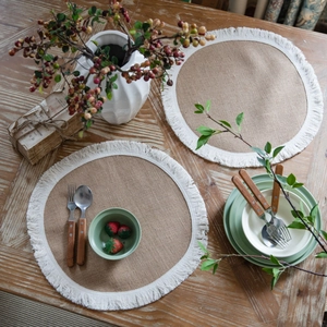 Natural jute round placemats with white cotton fringe on a rustic wooden dining table