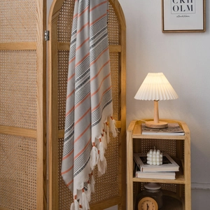 Nordic woven tablecloth with red stripes and fringe hanging on a rattan screen