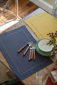 Detail view of cotton placemats with frayed edges and decorative white stitching on wood