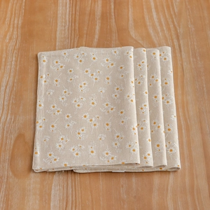 Set of four folded cotton linen placemats with daisy floral print on wooden table