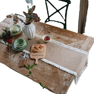 Natural jute table runner with white fringe tassels on a rustic wooden dining table