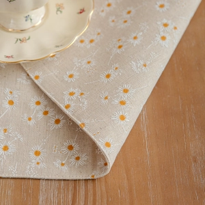 Linen placemat with white daisy floral embroidery on a light beige background