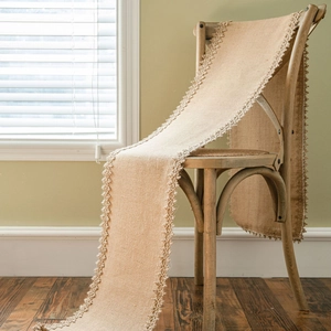 Natural jute table runner with cream lace trim draped on a wooden chair in a rustic room