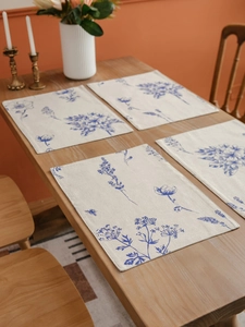 Detail of four cotton linen placemats with blue floral sketch prints on a wooden table