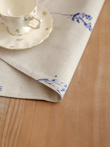 Close-up of linen-cotton placemat featuring blue floral sketch on rustic wood surface