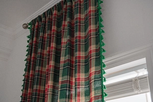 Detail of green and red plaid curtains with vibrant fringe trim and metallic ring hooks
