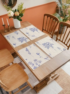 Detail of four rectangular linen placemats with blue floral prints on a wooden dining table