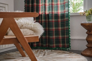 Close-up of green plaid curtain fabric with decorative fringe pom poms in a home setting