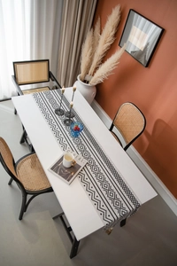 Détail d'un chemin de table à motifs géométriques avec pompons sur une table blanche