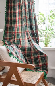 Detail of green plaid blanket with pom-pom fringe draped on a classic rattan chair