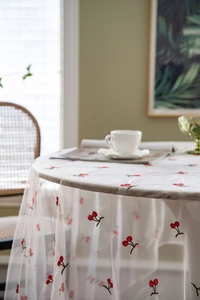 Close-up of white mesh tablecloth with delicate red cherry embroidery detail