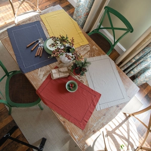 Fringed linen placemats in navy blue, yellow, red, and beige on a wooden table