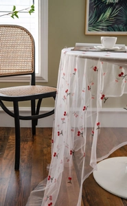 Detail of white sheer tablecloth with delicate red cherry embroidery in a rustic home setting