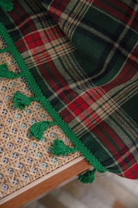 Detail of red and green plaid fabric curtains with tassels on woven rattan furniture