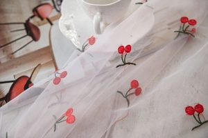 Detailed embroidery of red cherries on white mesh tablecloth for photography