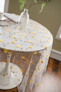 Macro detail of white mesh tablecloth featuring yellow 3D floral embroidery and green stems
