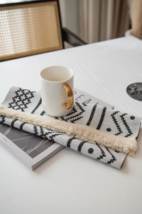 Vue détaillée du chemin de table bohème avec motifs géométriques et pompons beiges